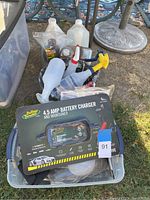 Photo showing boxed 4.5 Amp Battery Charger with other assorted household items in plastic tub outdoors on grass.