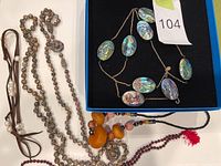 Blue box containing a necklace made of large oval abalone shell beads on a gold-colored chain, and a multicolored bead necklace with a variety of stone beads and a red tassel.