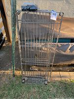 Disassembled chrome metal wire shelves stacked vertically outdoors on grass in sunlight.