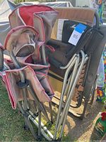 Three outdoor chairs folded and stacked: red and gray folding chair, beige zero gravity chair, and black Marlboro camp chair.