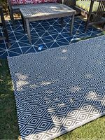 Both rugs shown partially overlapped outdoors, blue with white star pattern and black and white diamond pattern rug on grass.