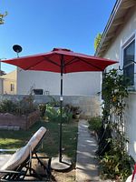Outdoor red patio umbrella fully open on its stand in backyard setting with greenery and patio furniture nearby.
