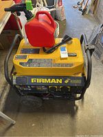 Generator front view with red gas can and spout on top, shows wheels and frame.