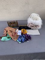 Photo of assorted clutches, white wedding bag with fur and floral detail, silk scarf, and flower hair clips on grey surface.