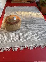 Photo of woven throw rug and round woven pouf placed on a red floor