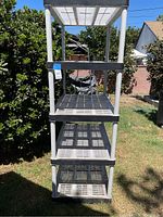 Full frontal view of the four-tier plastic shelving unit outdoors showing the grid pattern shelves and vertical supports.