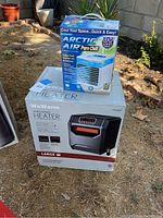 Photo of both the WeWarm space heater in its box and the Arctic Air Pure Chill cooler box outdoors on grass.