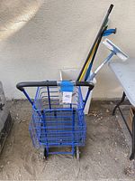 Front view of blue wheeled grocery cart with baskets and cleaning tools standing inside basket.