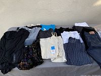 Top view of folded assorted women's tops including blouses, tunics, and tank tops in colors black, gray, blue, white, patterned fabrics.