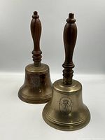 Two large brass bells with wooden handles placed side by side; both engraved with "Ford Citizen Bells" and a figure illustration