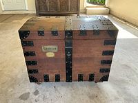 Front view of closed oak chest showing steel straps, corner plates and brass nameplate “S. Bircham.”