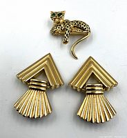 Front view of panther brooch and pair of geometric gold-tone earrings on white background