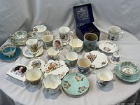 Overview of assorted cups, mugs, saucers and small porcelain items on white cloth