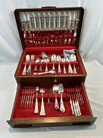 Wooden flatware chest open showing two drawers lined in red felt with flatware arranged