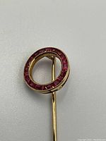 Front view of circular red gemstone-set head of gold stick pin