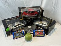 Overview of five boxed collectible car replicas including two Jaguar 3 coupes, one Volkswagen New Beetle, one BMW M Roaster, and one Porsche 928 with a green apple for size reference