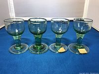 Front view of four green glass antique wine glasses with thick stems and bulbous bowls, showing old paper tags on two bases