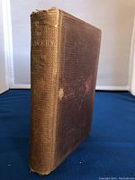 Side view of the antique book showing the textured brown cloth cover and wear on the spine and corners.
