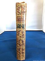 Close up side view of the antique book spine showing gold decorative floral embossing and text on leather binding.