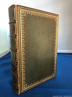 Antique leather bound book closed, showing detailed gold tooling on cover edges and spine with red leather labels