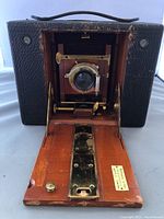 Front view of the antique wooden camera with its fold-down door open, showing leather bellows and brass lens.