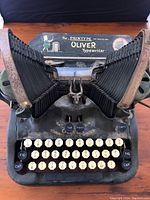 Front view of blue-black Oliver typewriter with twin bellows, cream keys, and gold lettering on body.