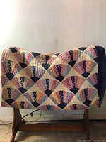 Wide view of the antique quilt draped over a wooden stand showing fan pattern blocks in various pastel printed fabrics with dark borders.