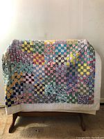 Antique patchwork quilt draped over a wooden stand, showing the full front view with colorful patchwork squares and cream border.