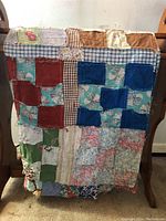 Full view of antique patchwork tablecloth draped over chair showing its multiple patterned and colored fabric patches.