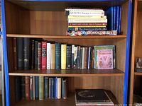 Wide view of three wooden bookshelf shelves showing quilting volumes on top, mixed fiction/non-fiction middle, vintage cloth bound bottom