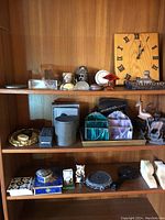 Photo showing assortment of clocks, figurines, paperweights, decorative wooden plaque, vintage tin, and desk organizers arranged on shelves