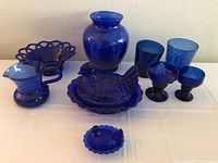 Full set of cobalt blue glassware including creamer, vase, candy dish, two glasses, two sorbet cups, and large and small hen on nest dishes.