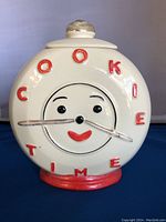 Front view of the vintage cookie jar shaped like a clock with 'COOKIE TIME' in red letters and a smiling face