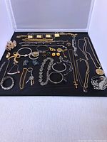 Full view of all assorted fashion jewelry laid on black cloth including brooches, necklaces, bracelets, earrings, and cufflinks.