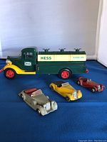 Photo showing vintage Hess gasoline tanker truck with three Dinky die-cast cars in front on a blue surface.