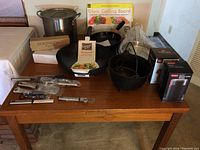 Overall set showing various kitchenware items on wooden table including large stockpot, wok, cutting board box, paper towel holder, coffee grinder boxes, utensils.