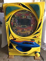 Front full view of the yellow Sanko pachinko machine with blue accents and circular display covered in plastic. Shows the machine's size and key features.