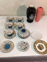 Five tea cups with blue bases and gold striped design, six matching saucers, covered bowl, and three decorative plates on a table.