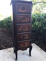 Full view of the tall narrow lingerie chest outdoors showing five drawers with painted scenes and ring pull handles.