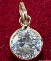 Close-up front view of the gold pendant showcasing the faceted round moissanite stone on a red background.