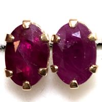 Close-up photo of pair of oval faceted deep red ruby earrings set in 10K gold with prong setting