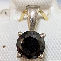 Close-up of the round black diamond pendant showing the stone and gold prongs.