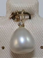 Close-up view of 14K gold pendant with white freshwater pearl and small diamond, showing pendant hanging in jewelry holder.