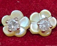 Close-up front view of two mother of pearl carved flower stud earrings with central round diamonds on red background.