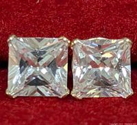 Close-up front view of two princess-cut cubic zirconia stones set in 9K gold earrings against red background.