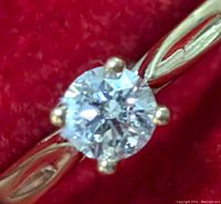 Close-up front view of 10K gold ring with round brilliant lab-created diamond set in four prongs against red velvet background.