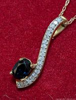 Close-up photo showing the gold pendant with oval sapphire and diamond accent stones.