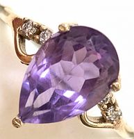 Close-up front view of pear-shaped purple natural amethyst center stone with diamond accents on 10K gold band