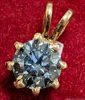 Close-up of round brilliant diamond set in 14K yellow gold six-prong pendant on red velvet