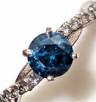 Close-up of round treated blue diamond centre and white diamond accents on twisted shank